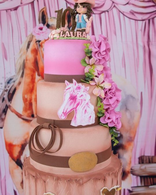 Bolo de aniversário de três andares com tema de cavalos e flores, na mesa decorada da festa.